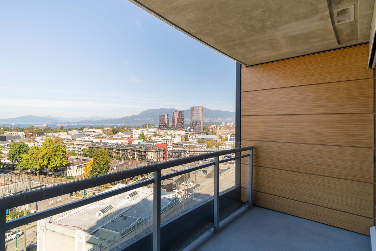 View from a high-rise balcony at 1565 West 6th Avenue, showing Vancouver’s skyline, roads, greenery, and distant mountains.