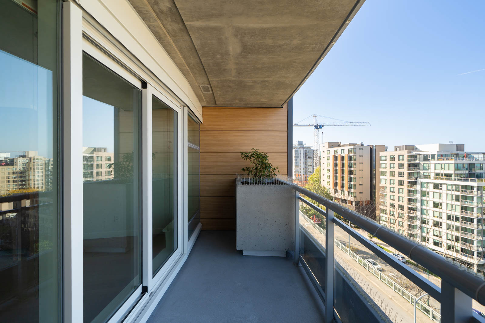 11th-floor balcony with glass doors, concrete planter with greenery, and city view under clear sky in Vancouver.