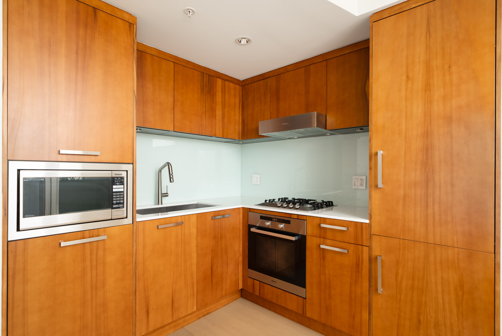 Modern kitchen with wood cabinets, built-in microwave, gas stove, oven, sink, and white backsplash in Vancouver.