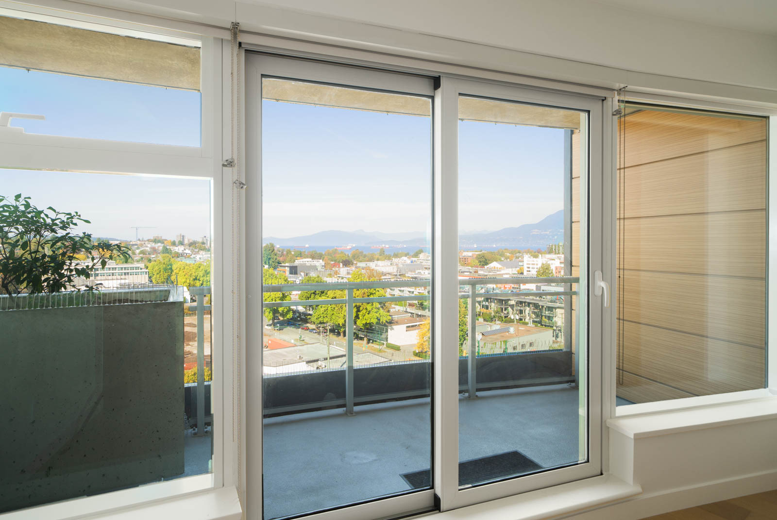 Glass doors lead to a balcony on the 11th floor at 1565 West 6th Ave, overlooking Vancouver, trees, buildings, and distant mountains.