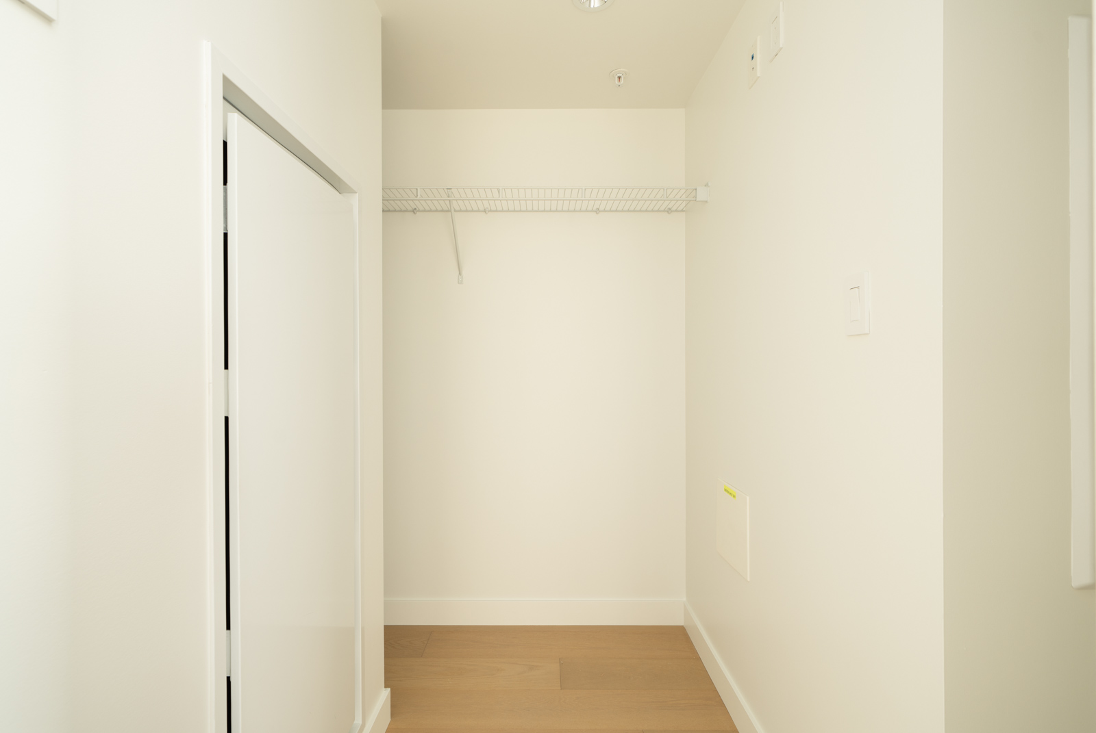 Empty walk-in closet at 1565 West 6th Ave, Vancouver with white walls, wire shelf, light wood floor, left door, right utility panel.