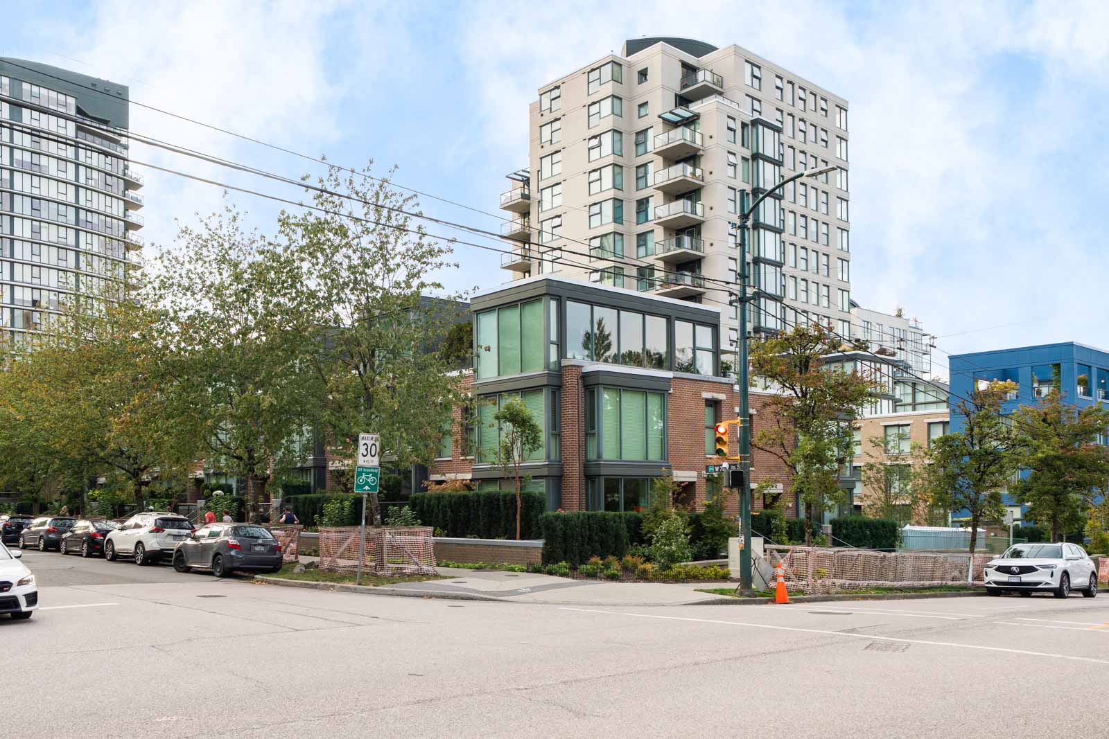 Urban street corner in Vancouver near 1428 West 6th Ave with apartments, cars, traffic lights, trees, and a speed limit sign.