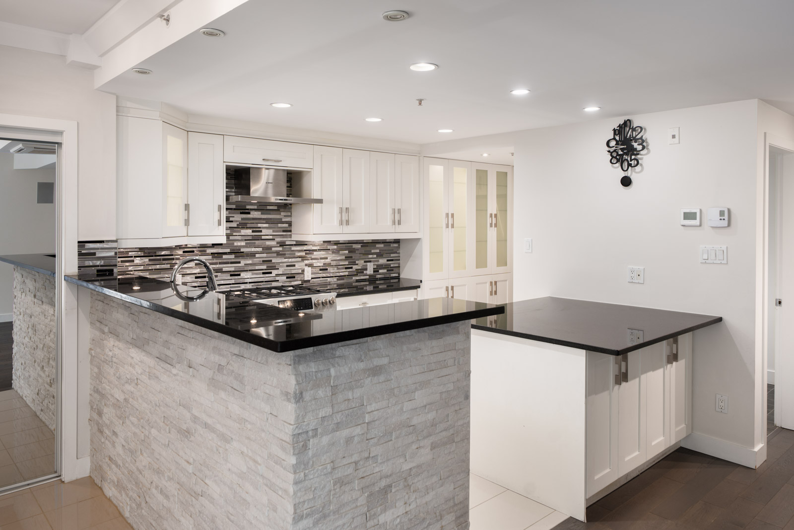 Modern kitchen at 1428 West 6th Ave, Vancouver with white cabinets, black counters, stone island, stainless appliances, mosaic backsplash.