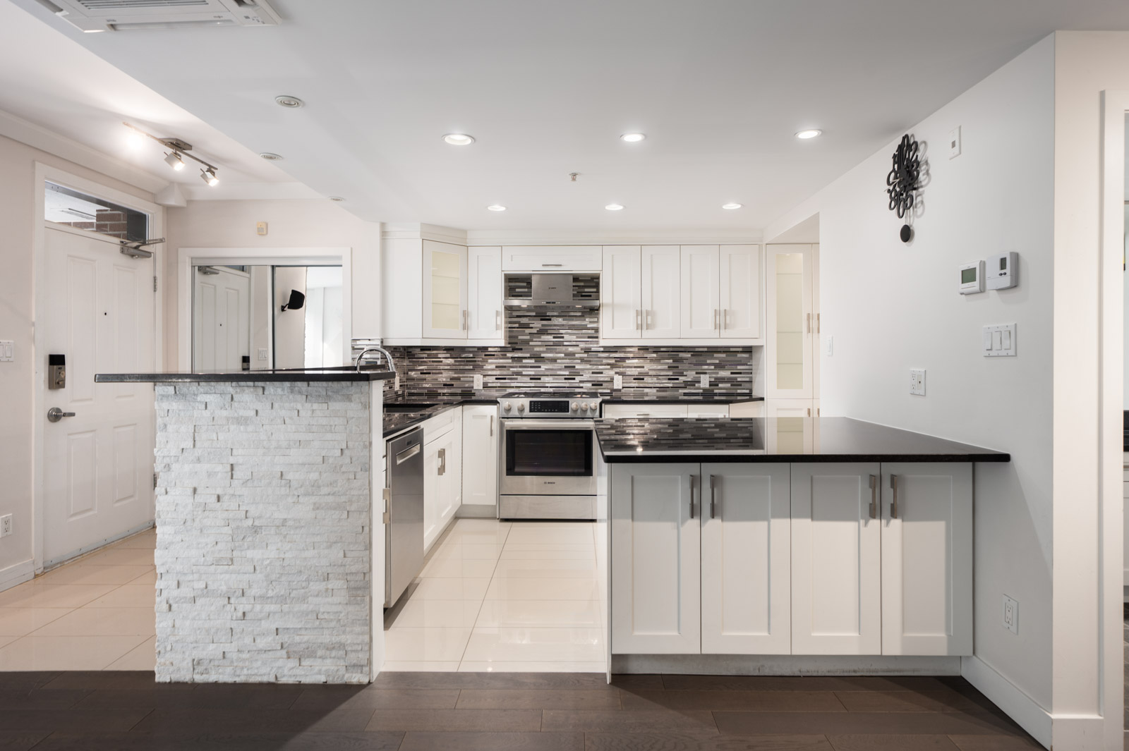 Modern kitchen at 1428 West 6th Avenue, Vancouver, with white cabinets, black countertops, stainless appliances, and tile backsplash.