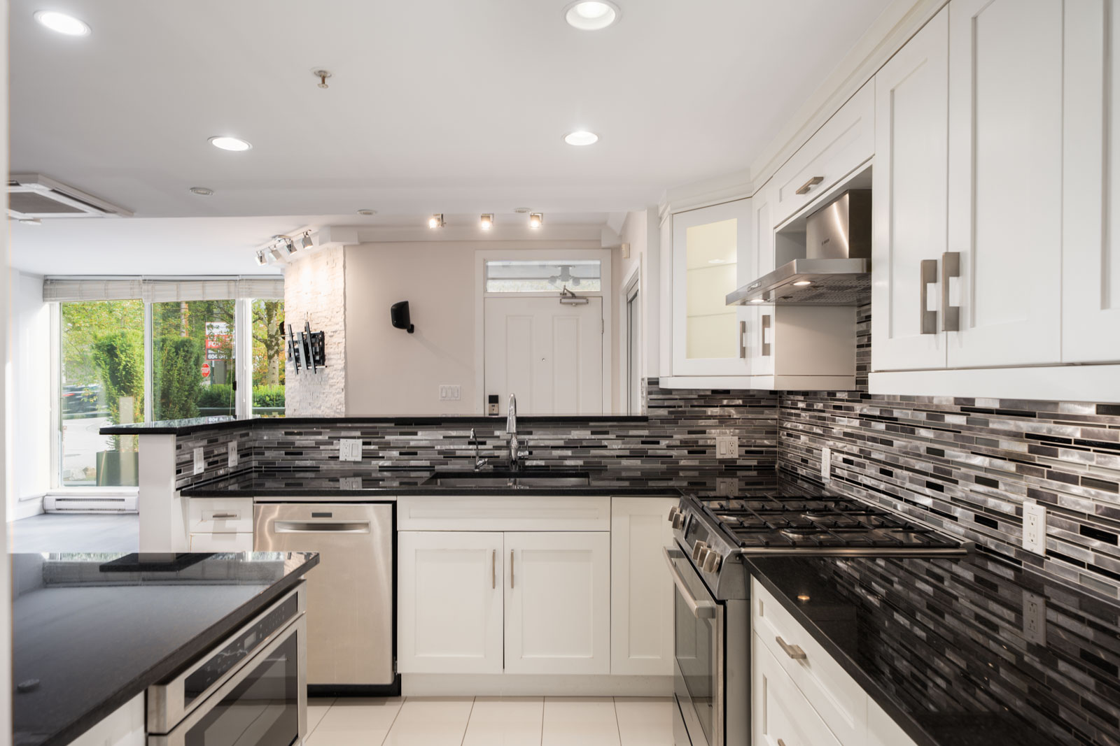 Modern kitchen at 1428 West 6th Ave, Vancouver with white cabinets, black countertops, stainless appliances, and large windows.