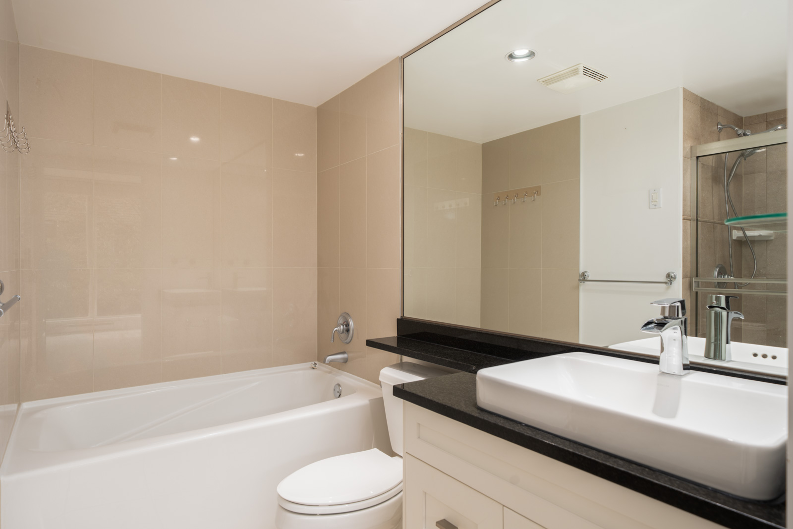 Modern Vancouver bathroom with white bathtub, toilet, large mirror, countertop sink, and glass-enclosed shower in back.