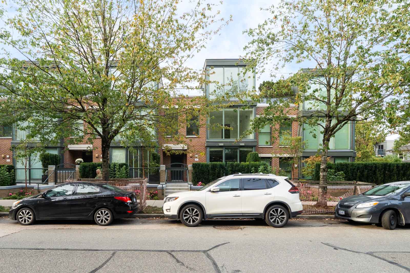 Three cars parked on a residential street outside modern brick townhouses at 1428 West 6th Ave, Vancouver, with large windows and trees.