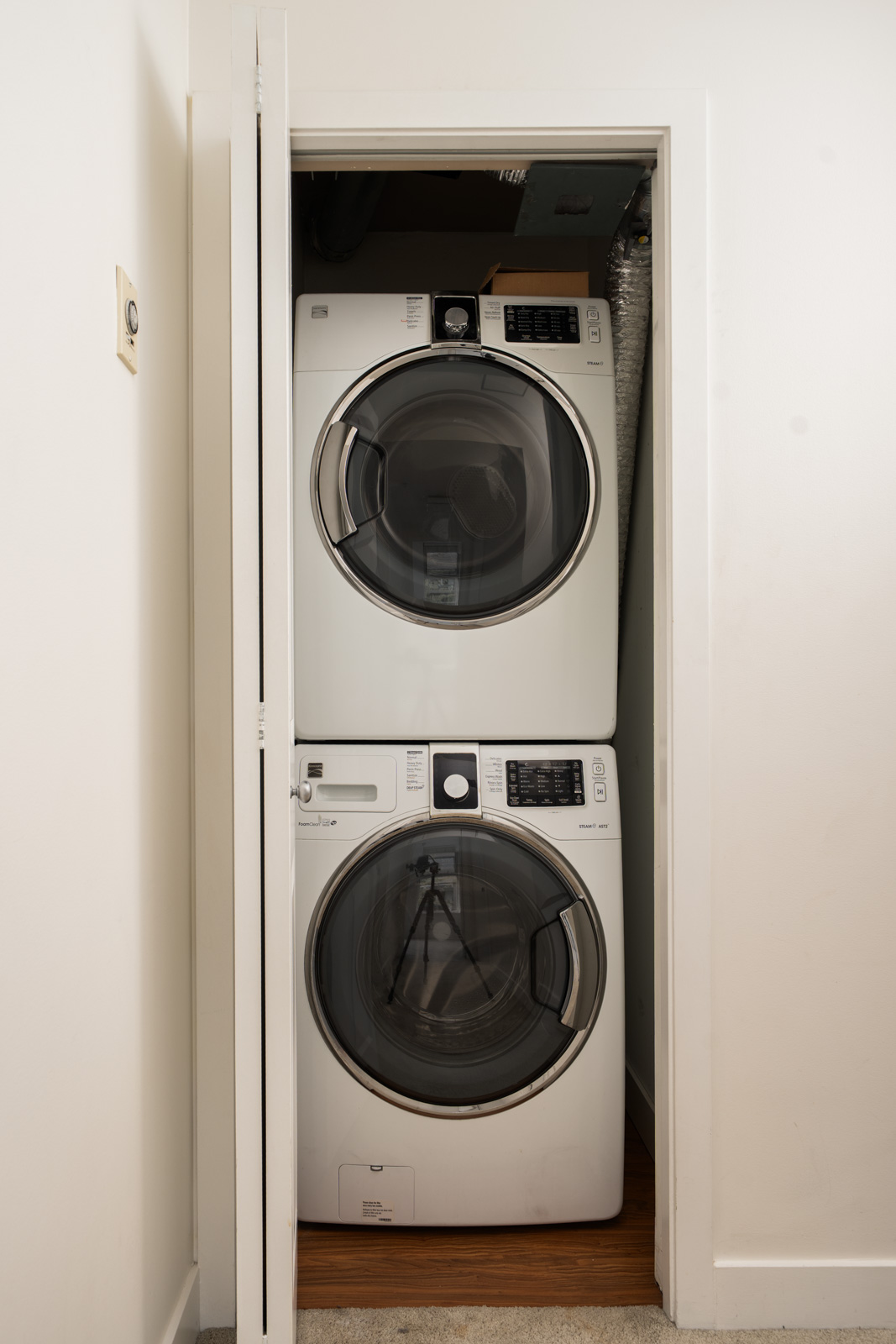 A stacked front-loading washer and dryer sit in a small white closet with an open bi-fold door in a Vancouver townhouse.
