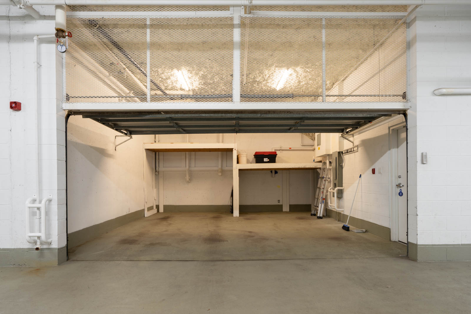 Open two-car garage with white walls, shelves, red toolbox, ladder, broom, and overhead lights at 1428 West 6th Ave, Vancouver.