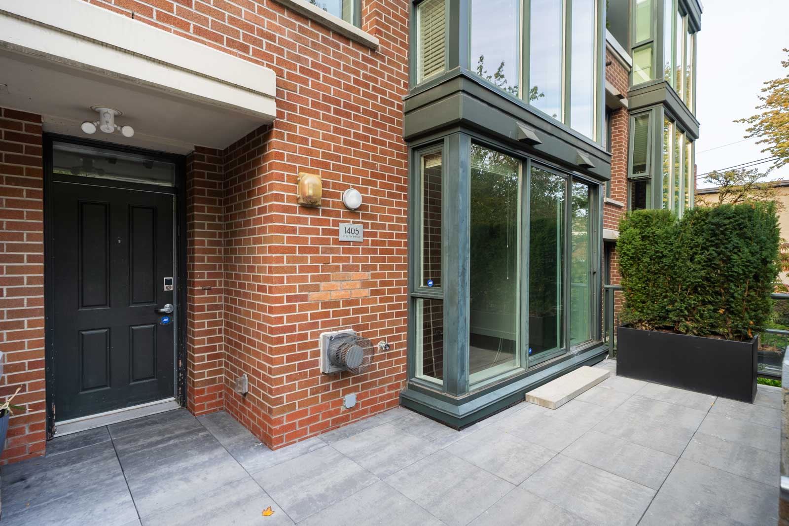 Ground-level entrance to a modern brick townhouse at 1428 West 6th Avenue, Vancouver, with large windows and a black door.