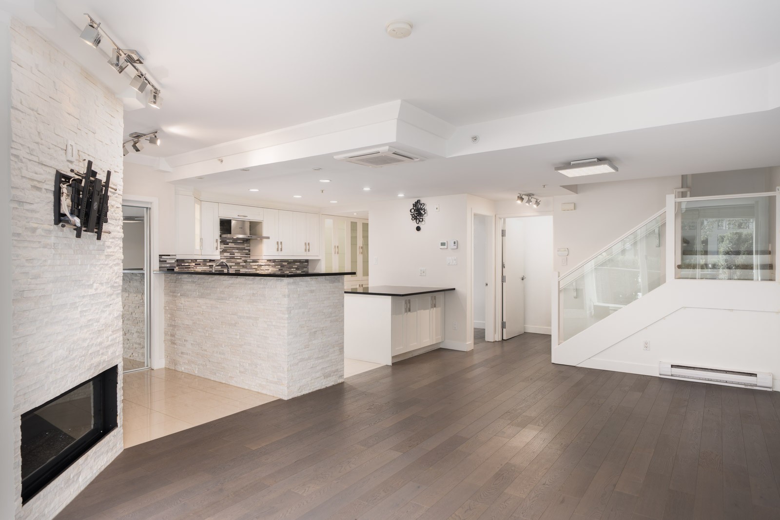 Unfurnished modern townhouse at 1428 West 6th Ave, Vancouver with dark hardwood floors, white kitchen, fireplace, and glass railing.