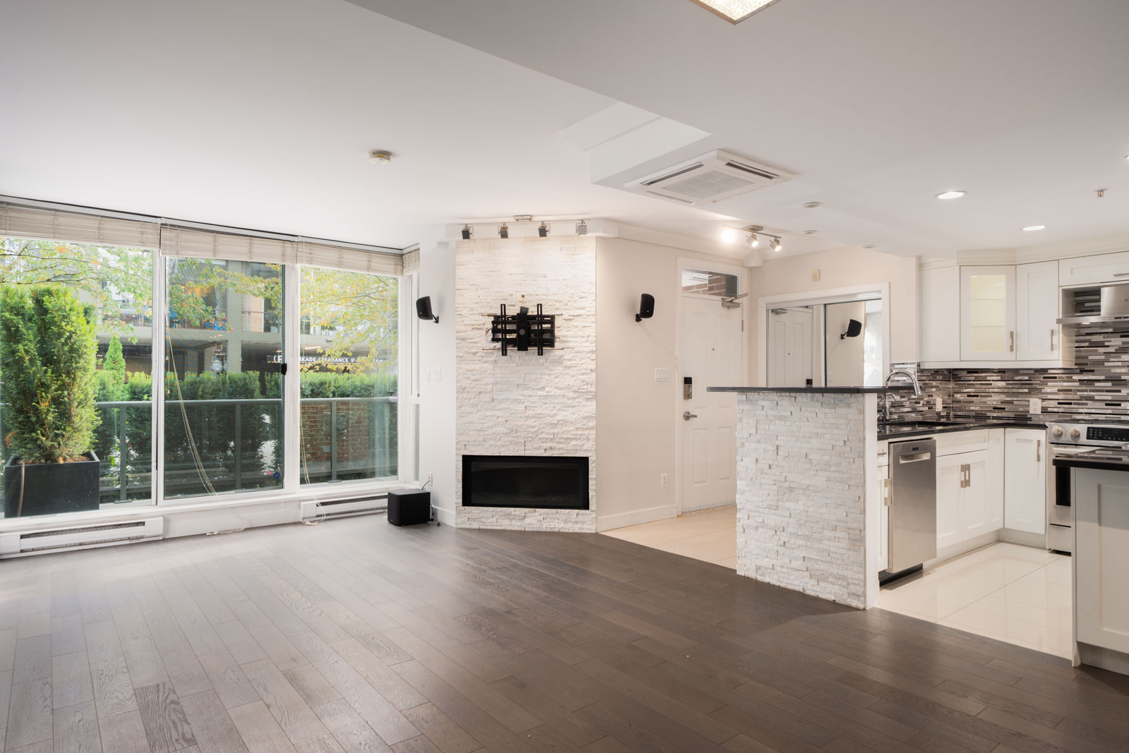 Modern open-concept living area in a Vancouver townhouse with dark hardwood floors, large windows, stone accent wall, and white kitchen.