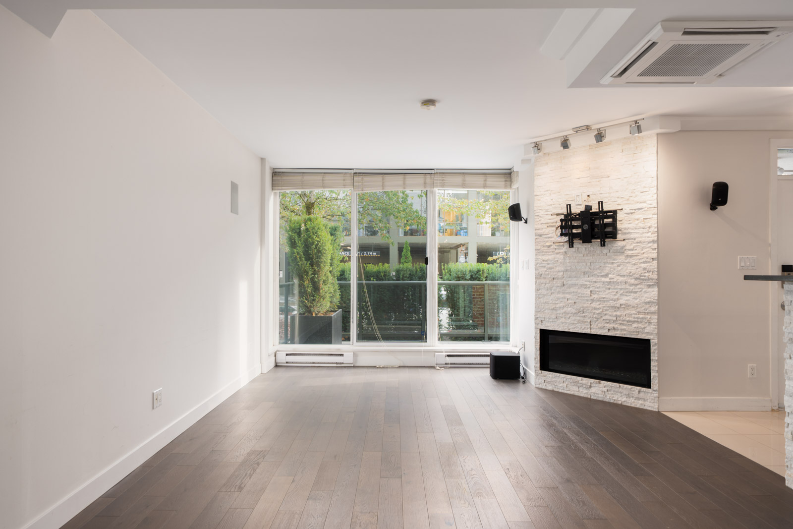 Bright living room at 1428 West 6th Ave, Vancouver, with large windows, white walls, dark wood floors, and views of trees.