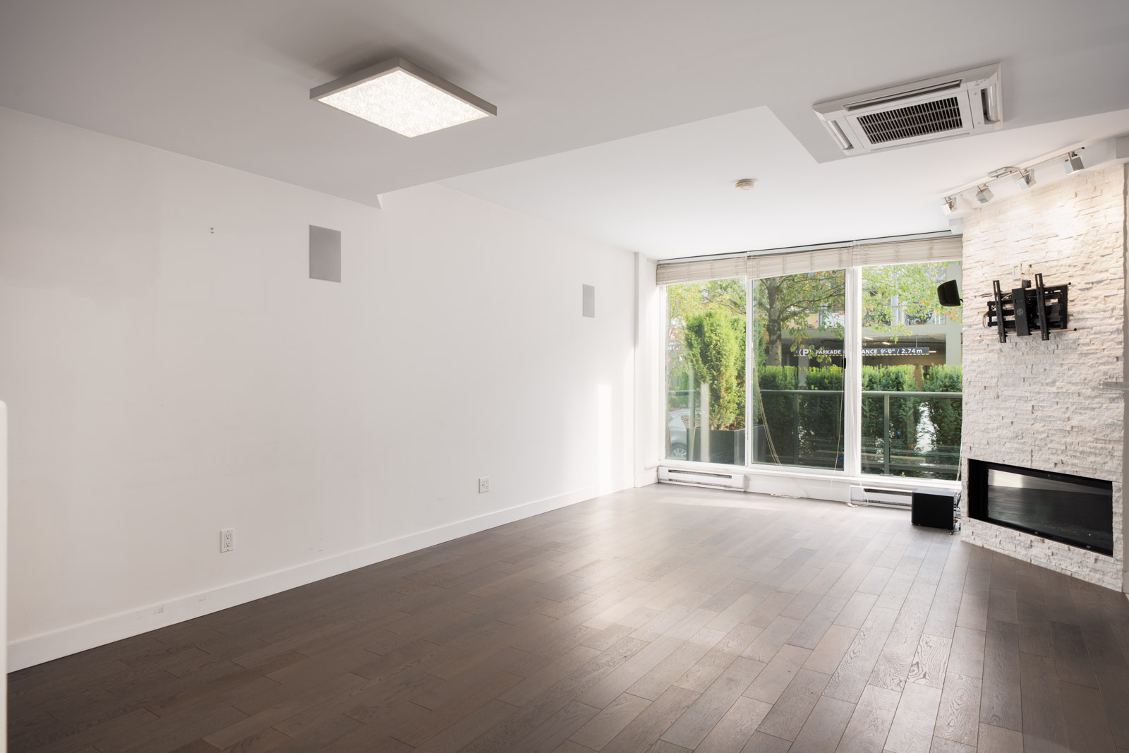 Modern townhouse living room in Vancouver with dark wood floors, white walls, large windows, and a stone fireplace.