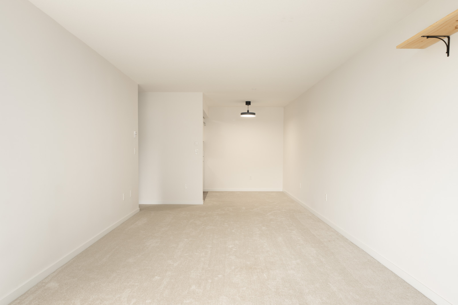 Empty room at 2245 Wilson Ave, Port Coquitlam, with beige carpet, white walls, ceiling light, and a small shelf on the right.