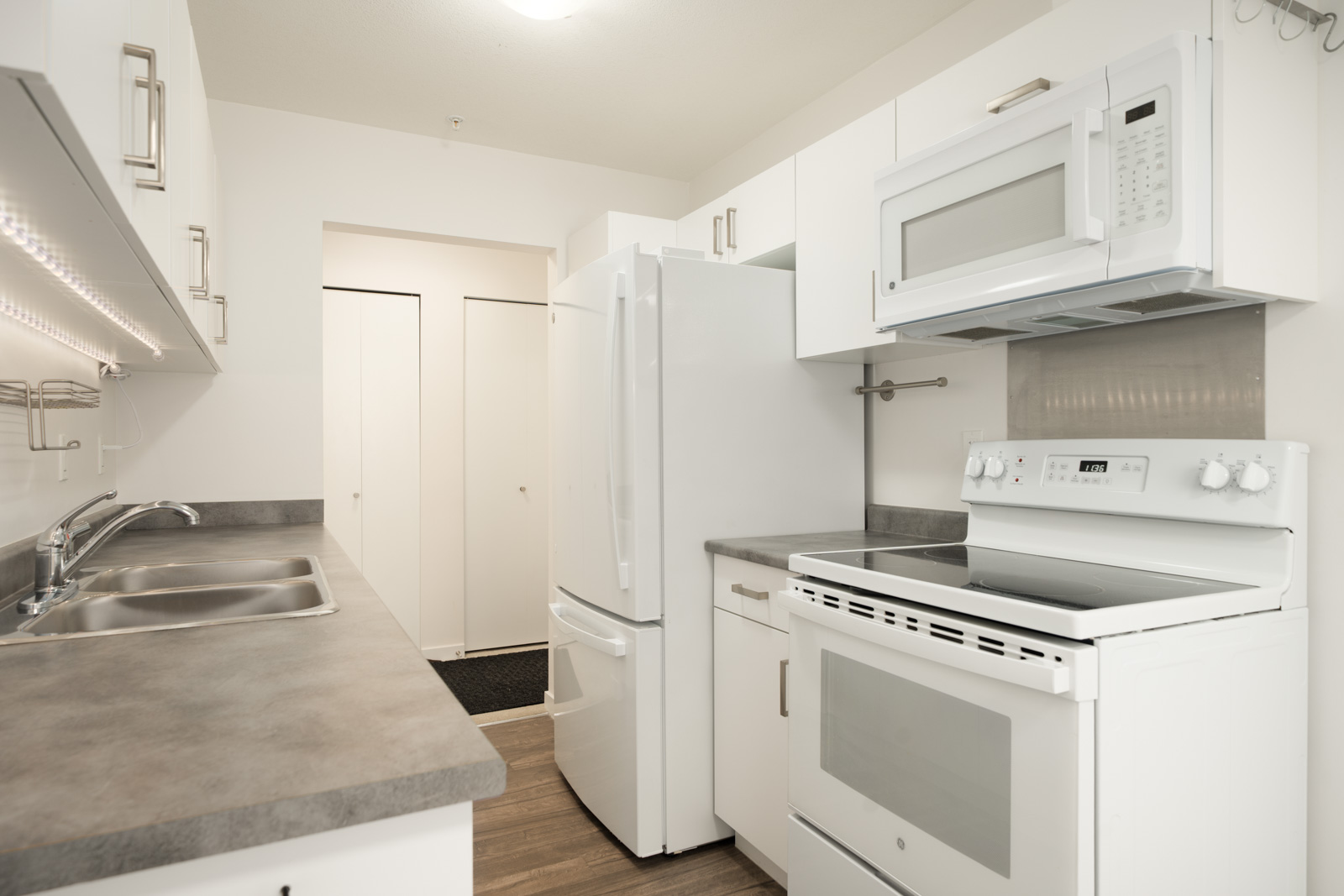 Modern kitchen at 2245 Wilson Ave, Port Coquitlam with white cabinets, gray counters, double sink, and wood floors to closet.