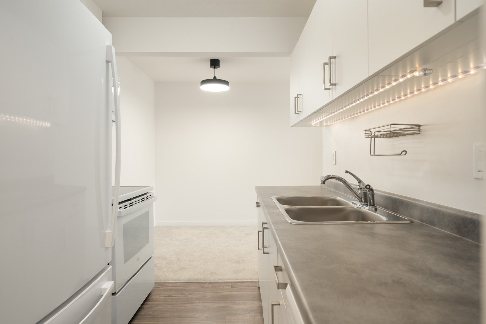 Modern kitchen with white cabinets, stainless sink, electric stove, fridge, under-cabinet lighting on 3rd Floor, 2245 Wilson Ave, Port Coquitlam.