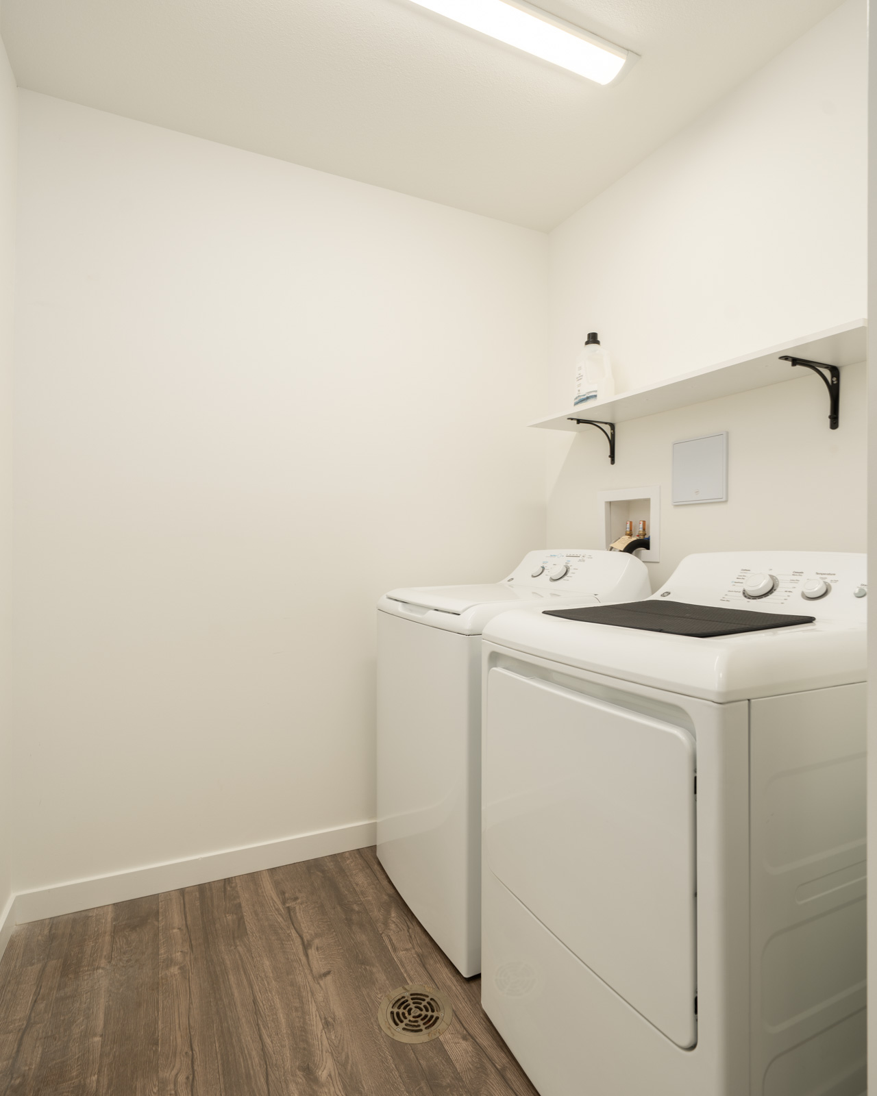 Laundry room at 2245 Wilson Ave, Port Coquitlam with side-by-side washer and dryer, shelf with detergent, wood-look flooring.
