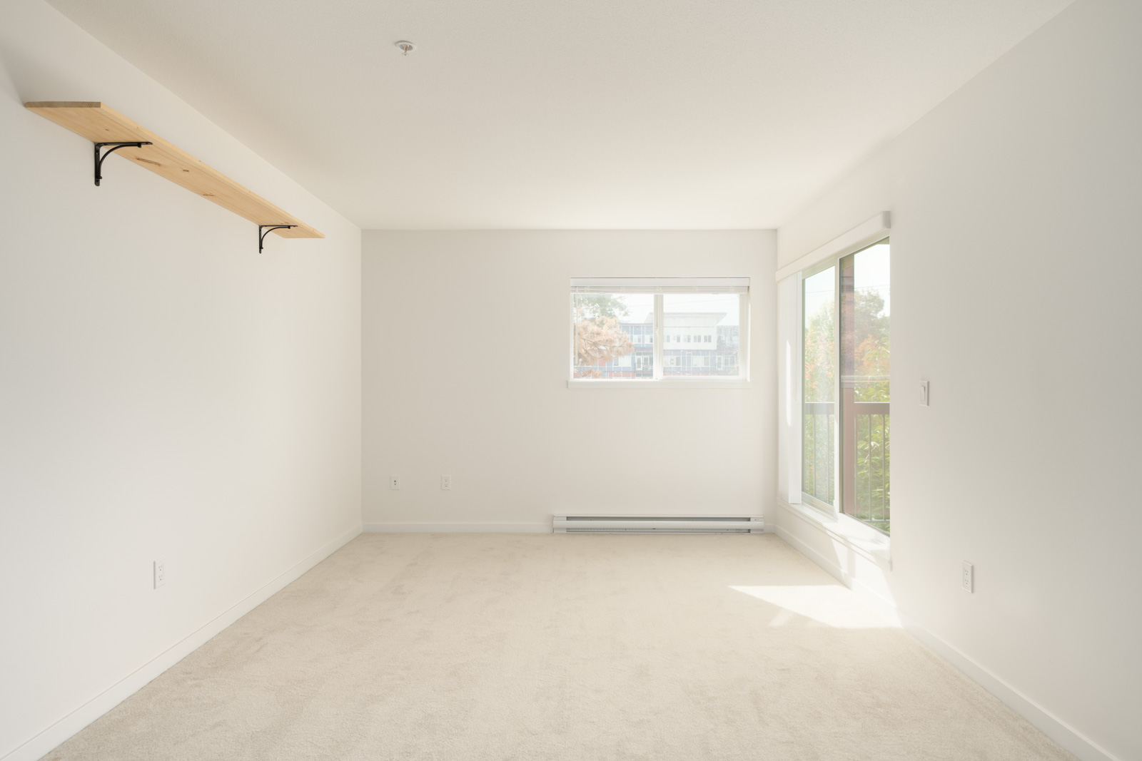 Empty room with white walls, beige carpet, wood wall shelf, window, and glass door on 3rd floor at 2245 Wilson Ave, Port Coquitlam.