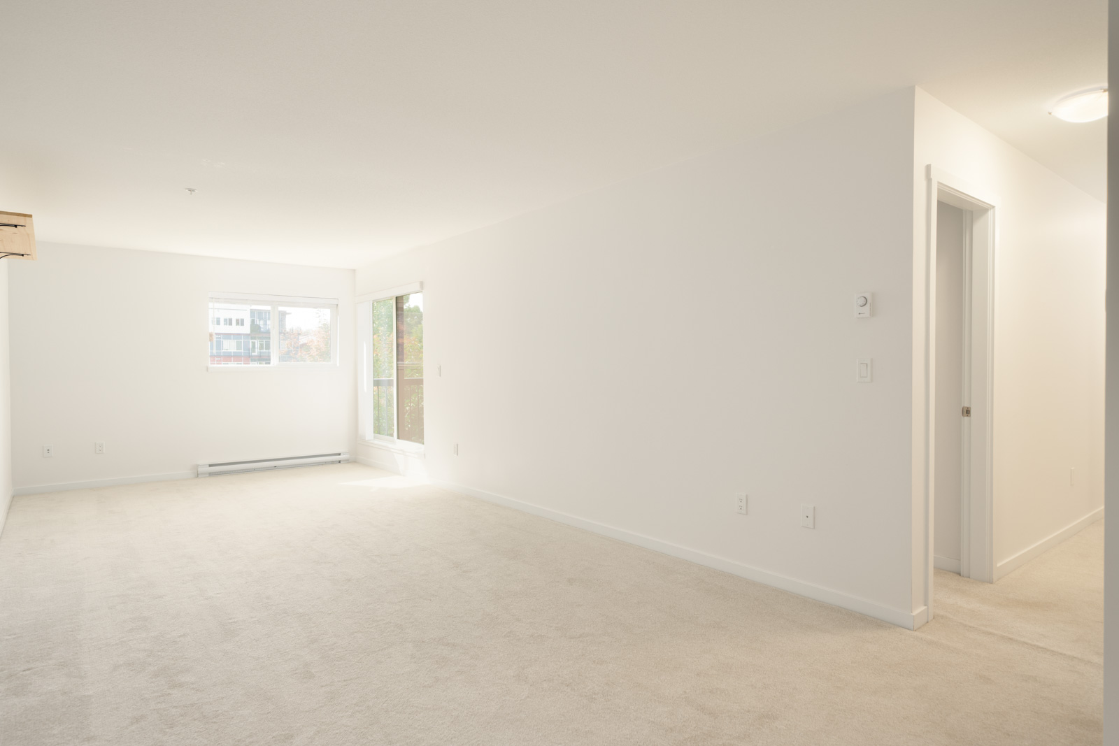 Empty living room at 2245 Wilson Ave, 3rd Floor, Port Coquitlam with beige carpet, white walls, large window, and glass door.