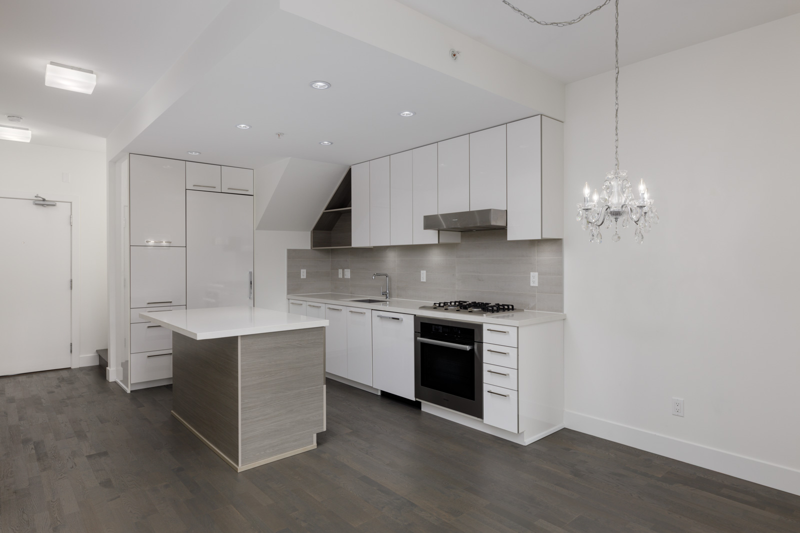 Modern kitchen on 4th floor, 1628 W 4th Ave, Vancouver: white cabinets, built-in appliances, island, grey wood floors, chandelier.