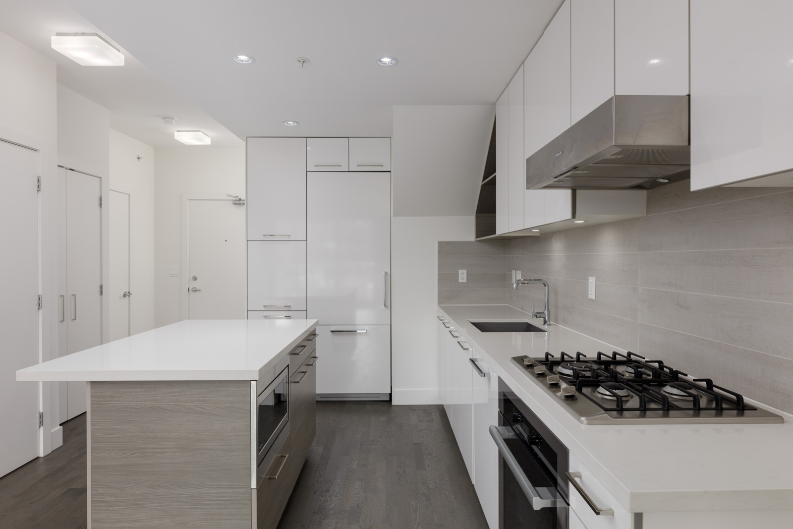 Modern kitchen at 1628 W 4th Ave, Vancouver, with white cabinets, built-in appliances, gas cooktop, island, and grey wood floors.