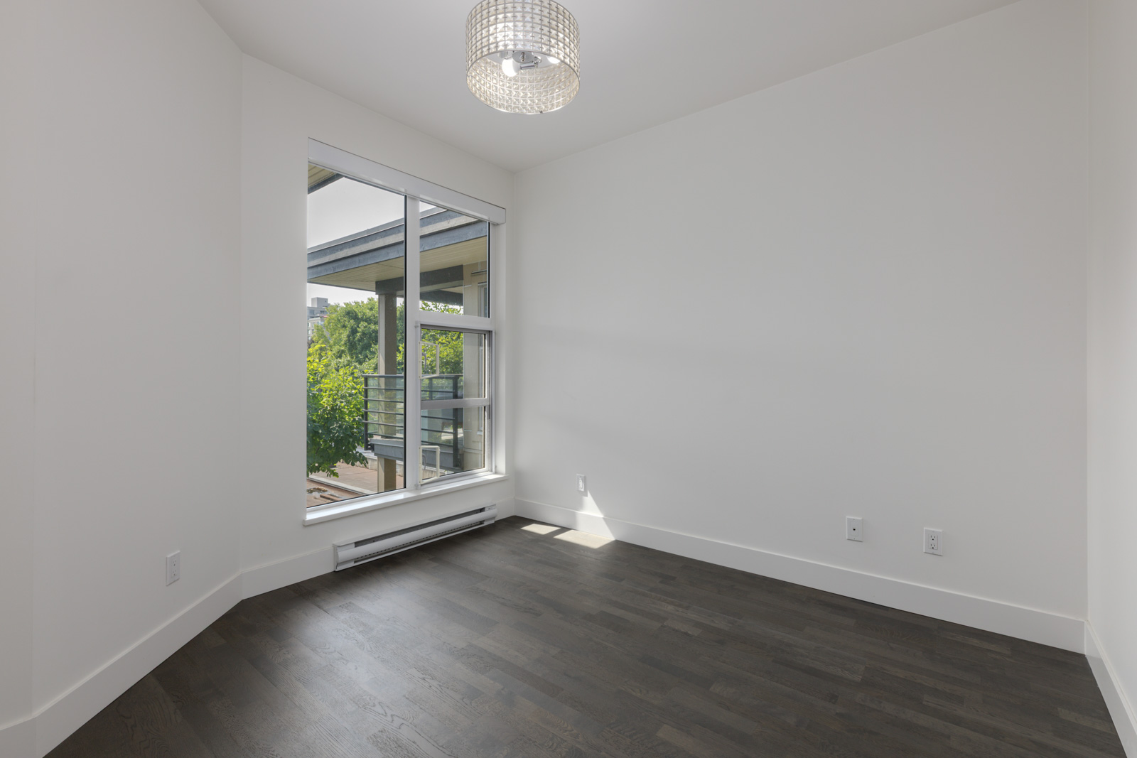 Empty room with white walls, dark wood floor, large window overlooking Vancouver, and ceiling light on the 4th floor of 1628 W 4th Ave.
