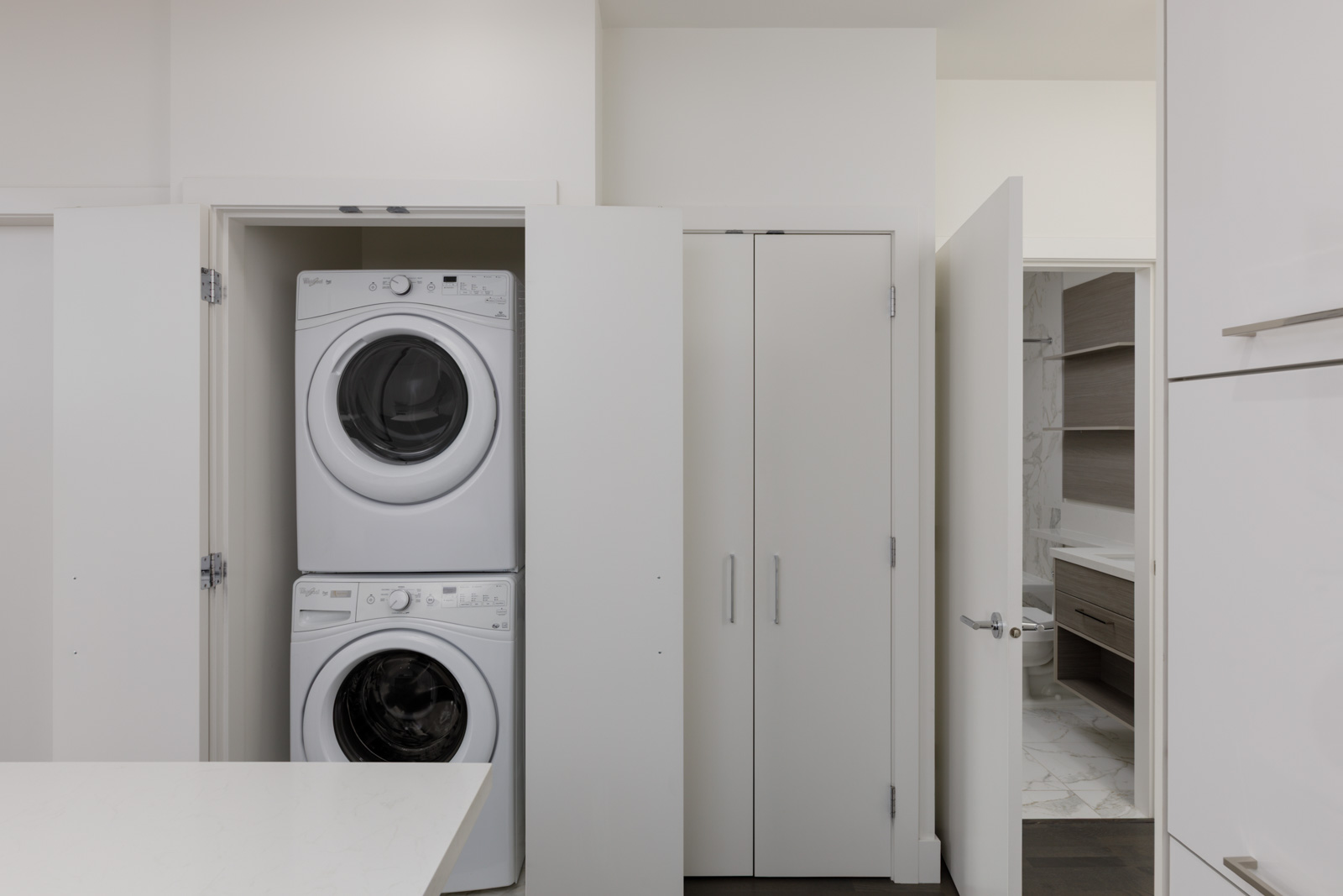 A stacked washer and dryer sit in an open closet within a modern laundry room with white walls on the 4th floor, 1628 W 4th Ave, Vancouver.