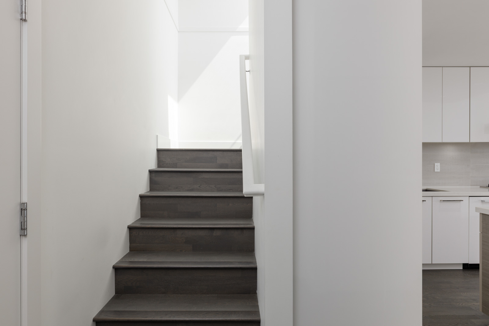 Minimalist staircase with dark wood steps and a white handrail, ascending by a white wall to the 4th floor at 1628 W 4th Ave, Vancouver.