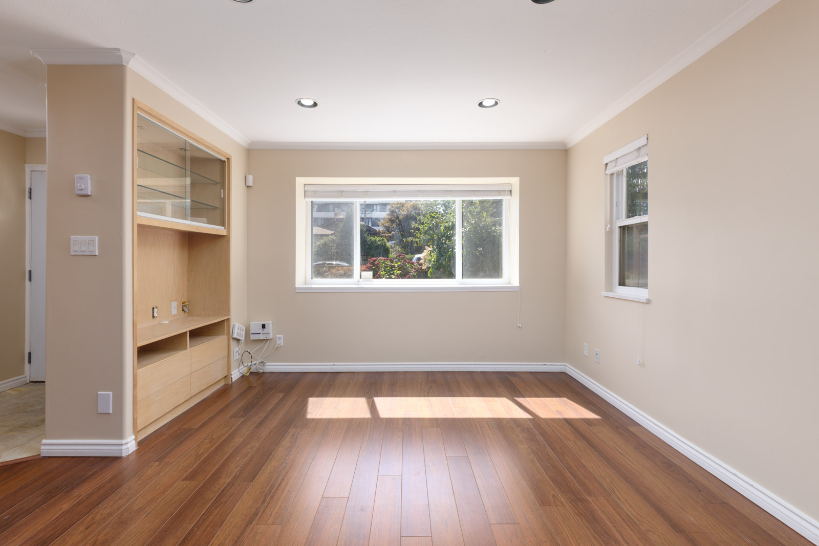 Empty living room with wood floors, built-in shelves left, large back window, small side window; near West 8th Ave, Vancouver.