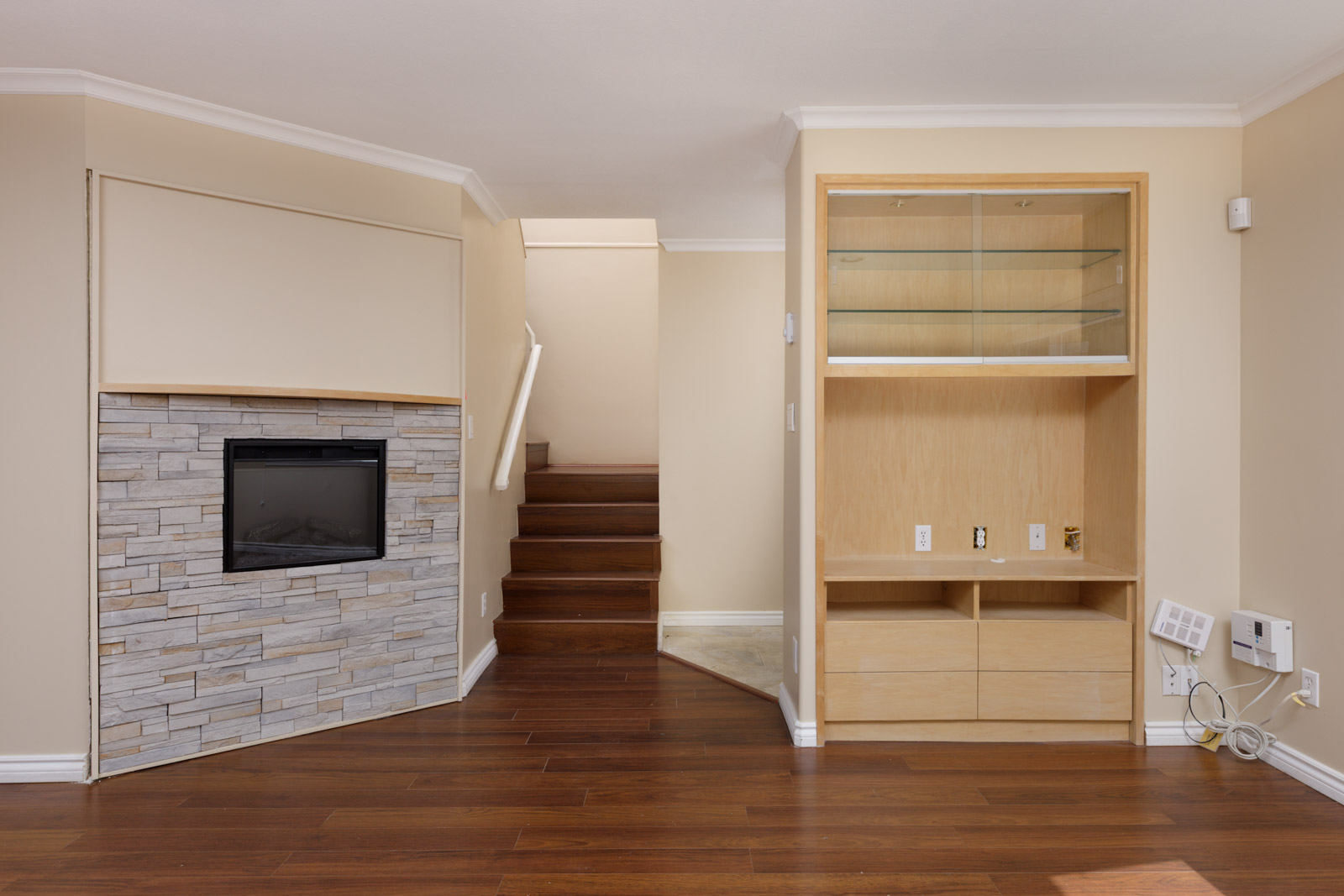 Modern living space with wood floors, built-in shelves, stone electric fireplace, stairs, neutral walls near Musqueamview St, Vancouver.