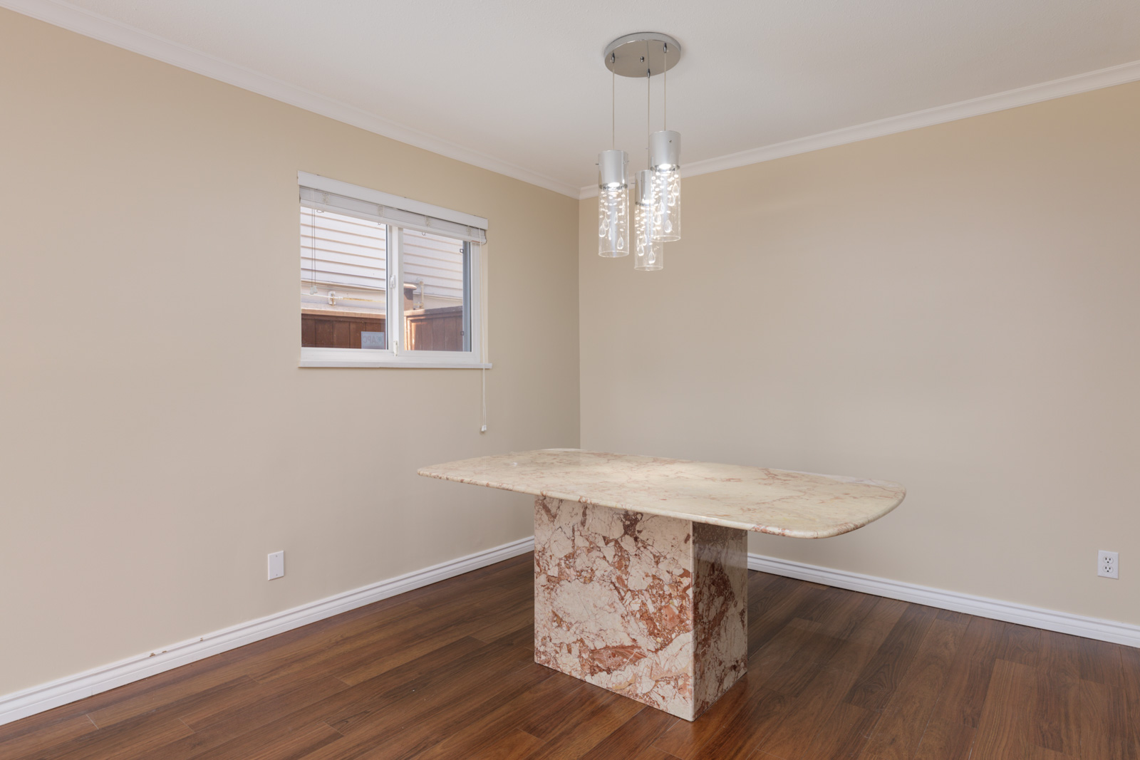 Empty room on West 8th Ave, Vancouver, with beige walls, marble table, wood floor, window blinds, and modern ceiling light.