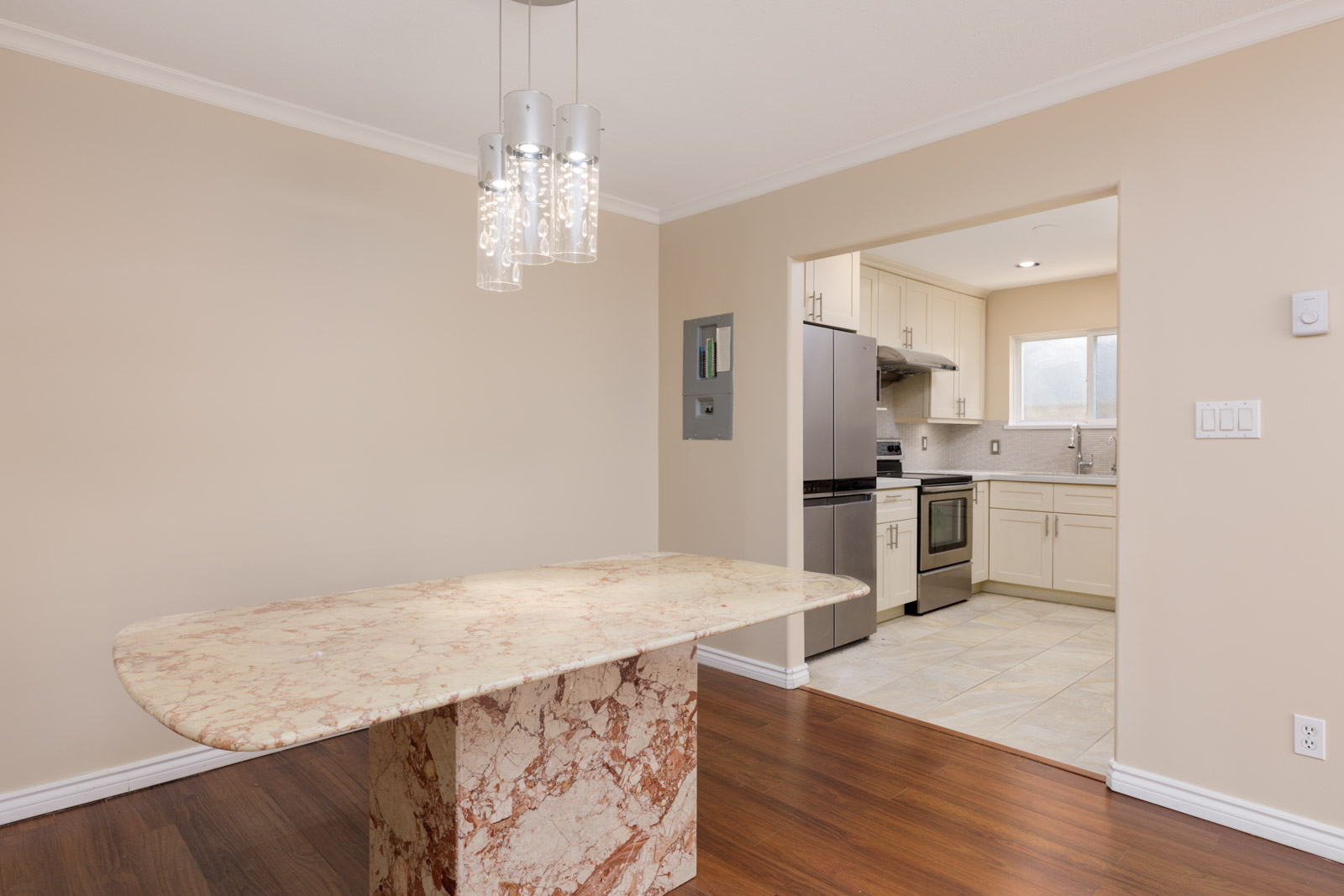 Dining area with marble table, wood floor, three pendant lights, and view of a kitchen with stainless appliances in Vancouver.