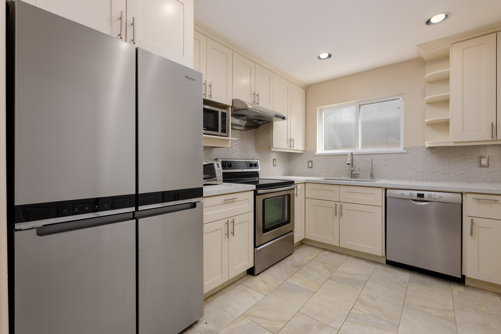 Modern kitchen with stainless steel appliances, cream cabinets, tile floor, built-in microwave, window over sink near Vancouver’s West 8th Ave.