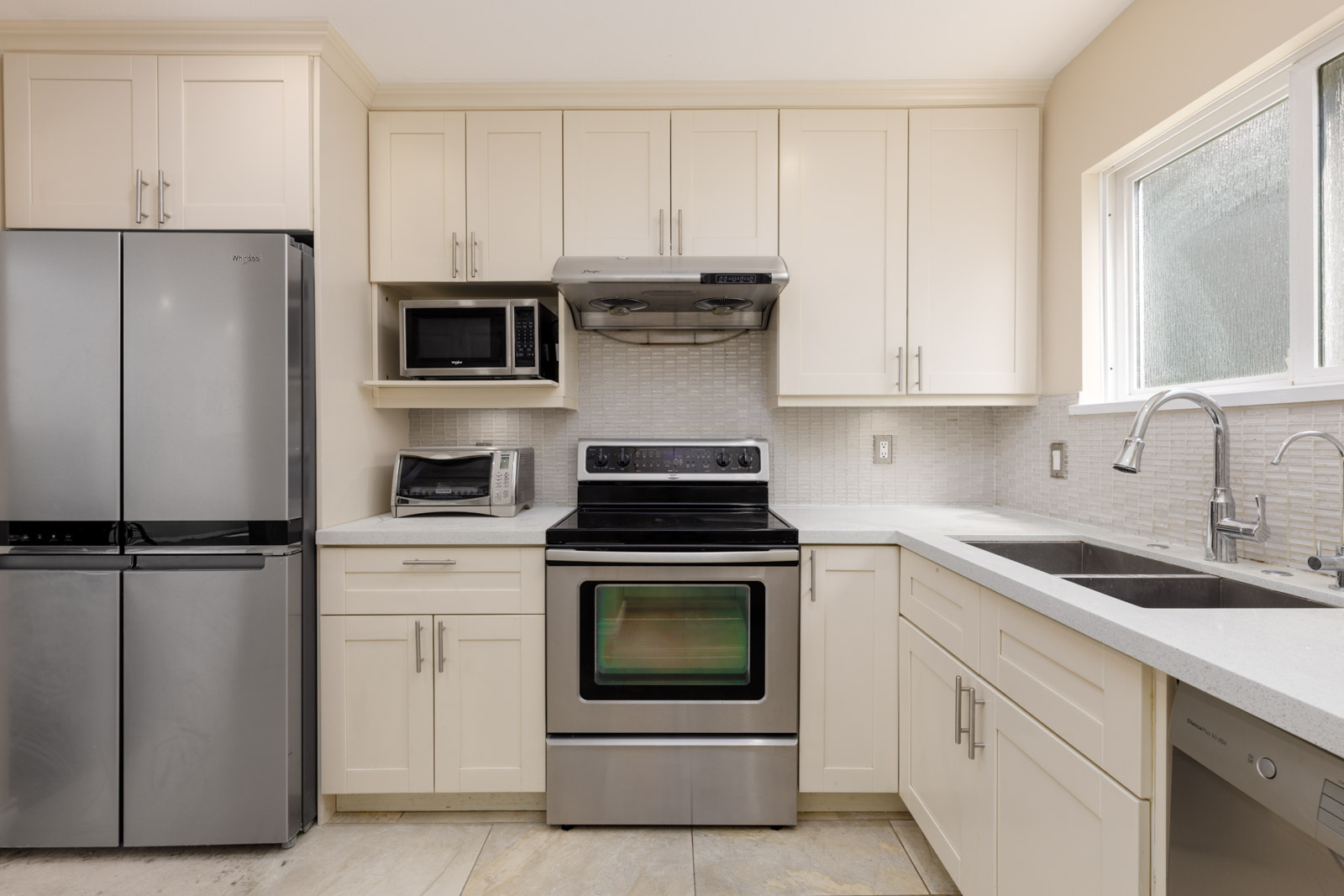 Modern kitchen on Musqueamview St with stainless steel appliances, white cabinets, and a window facing Vancouver’s West 8th Ave.