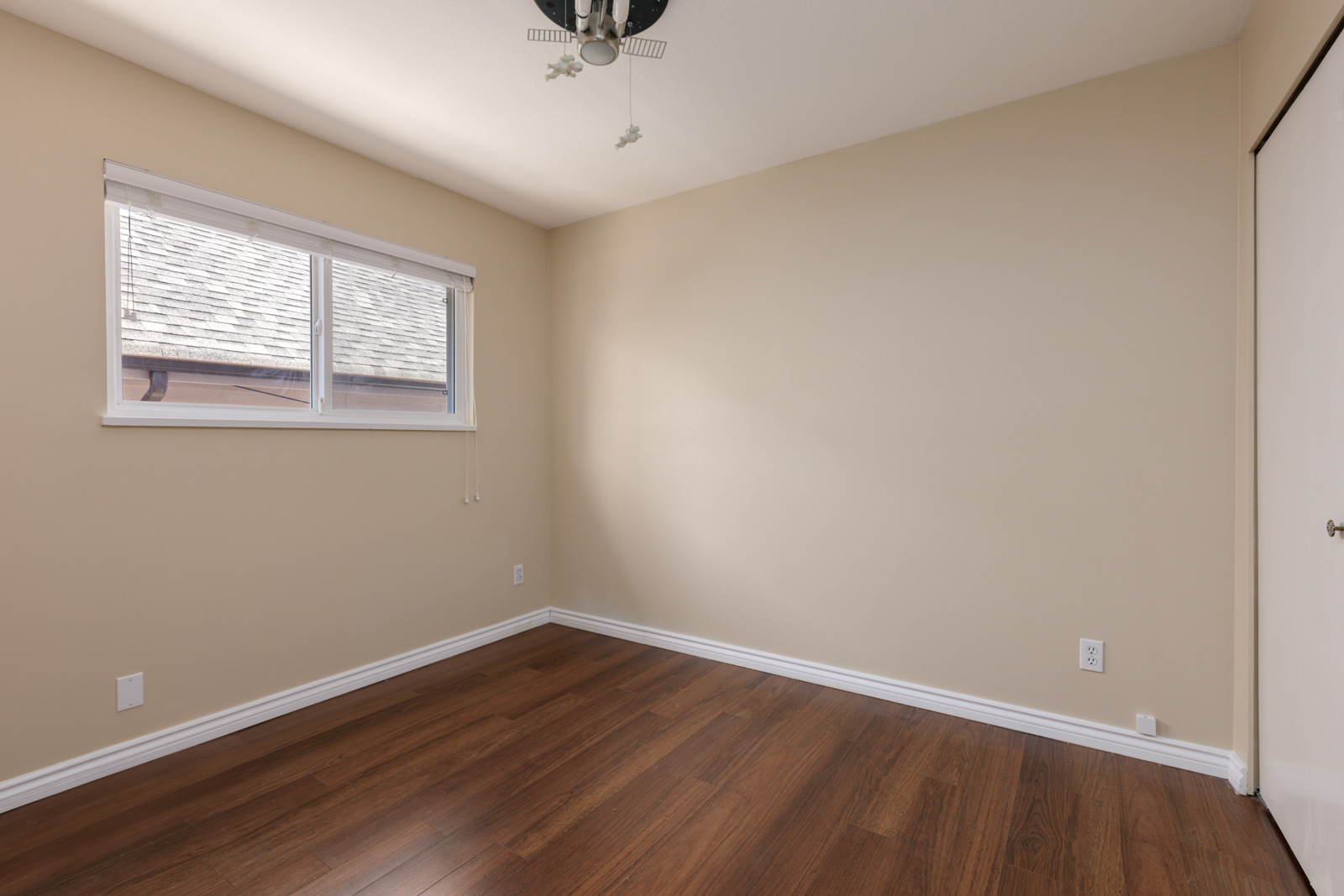 Empty room with beige walls, wood floors, window blinds, ceiling fan, and white sliding closet door near West 8th Ave, Vancouver.