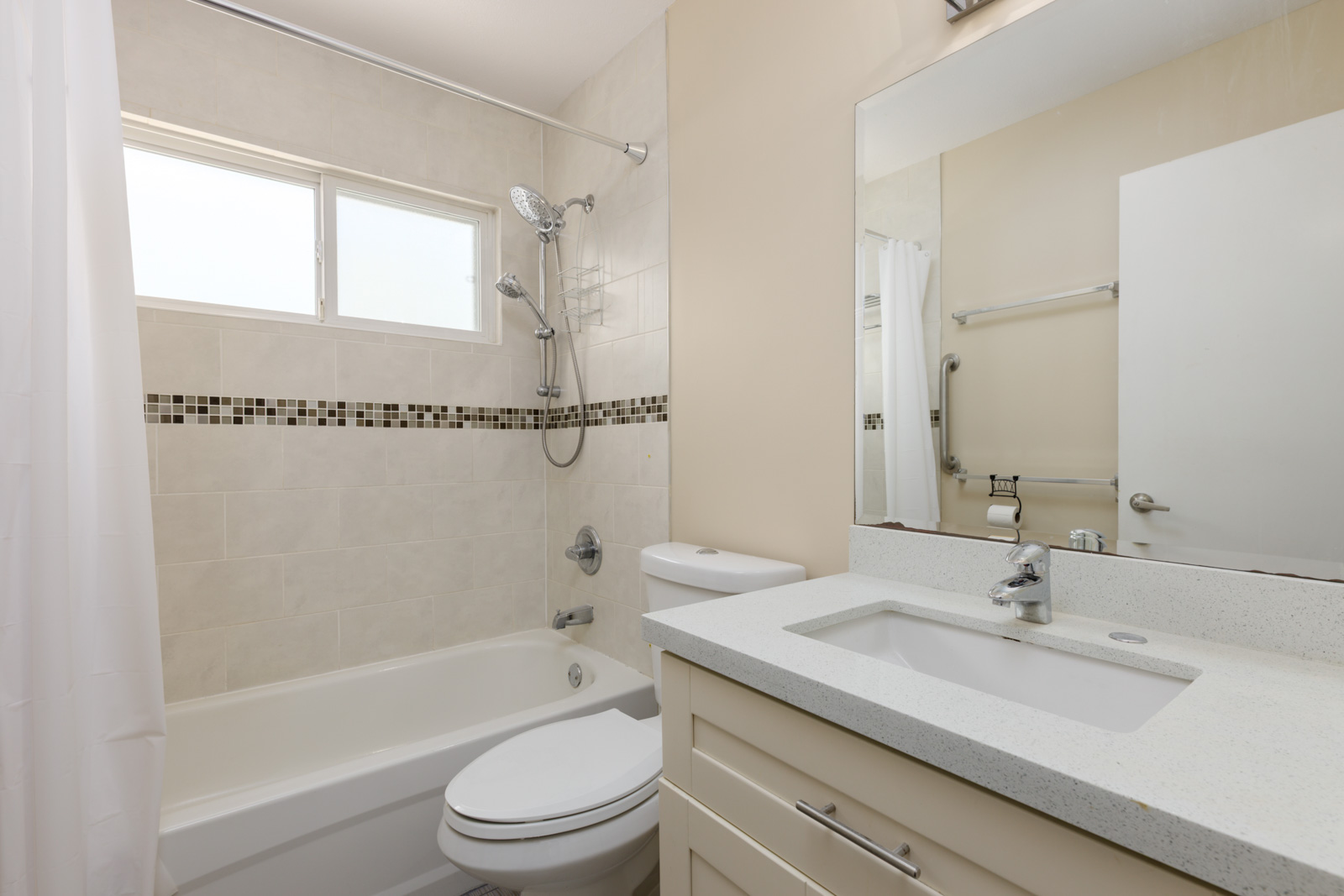 Modern bathroom in a West 8th Ave duplex with white tub, shower, toilet, vanity, large mirror, neutral tiles, and window above tub.