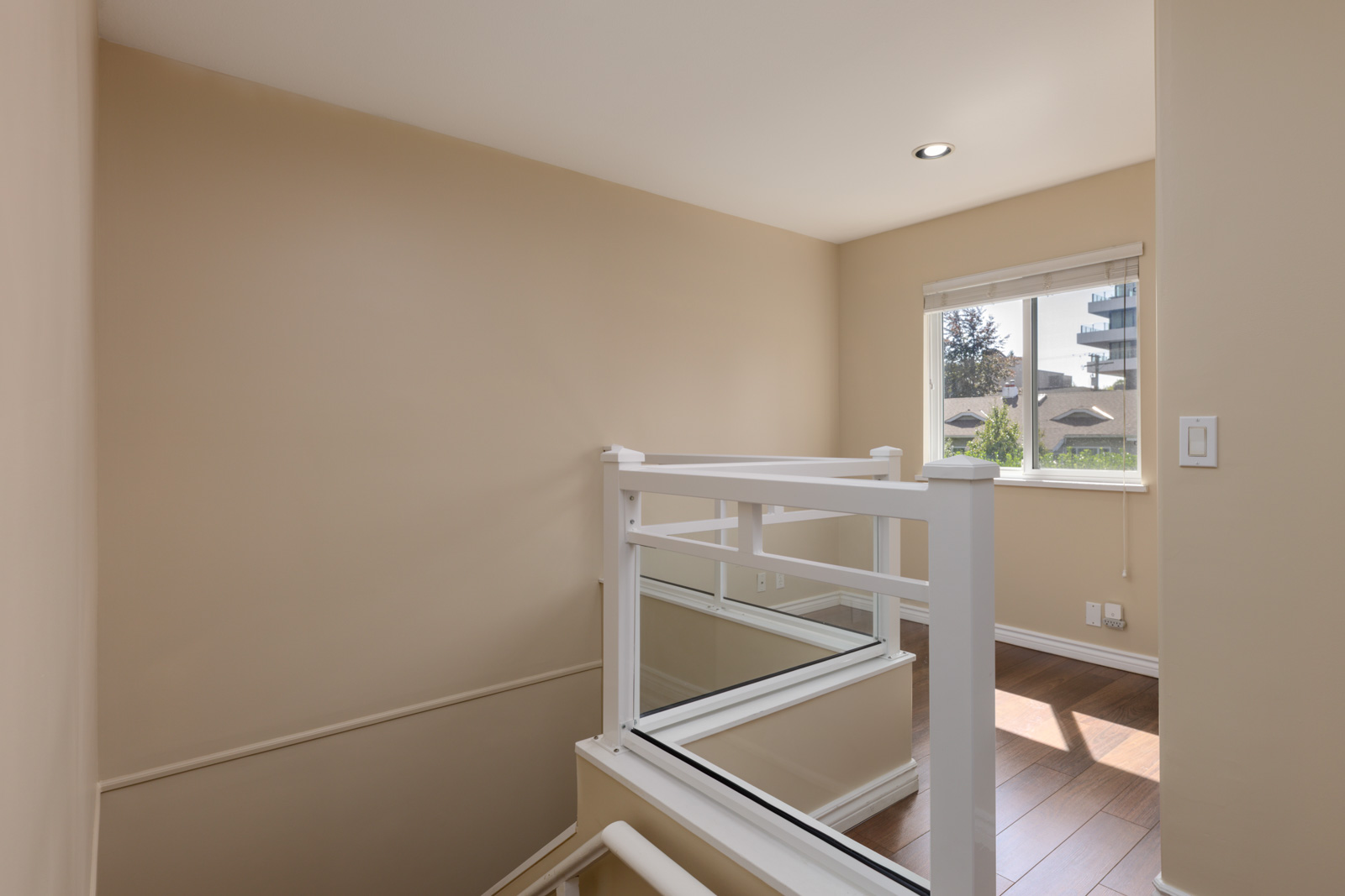 Small stair landing with beige walls, white railing, hardwood floor, and window with natural light in a Vancouver home.