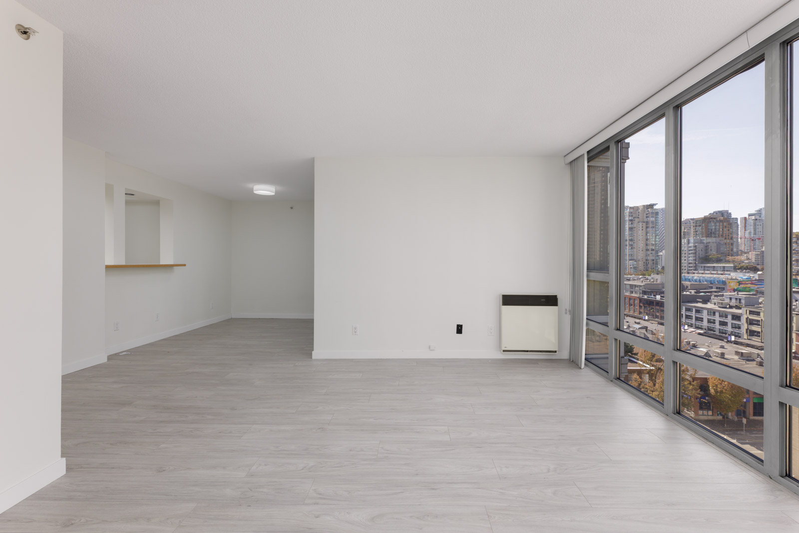 Unfurnished living area with light wood floors, large windows, white walls, and city views at 950 Cambie St, Vancouver.