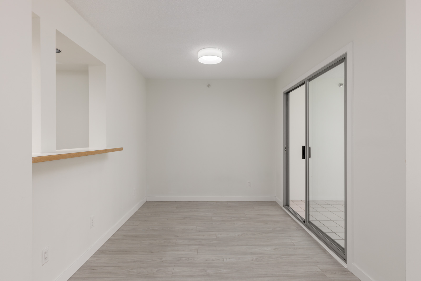 Empty room at 950 Cambie St, Vancouver, with light gray wood floors, white walls, sliding glass doors, and a cutout window with ledge.