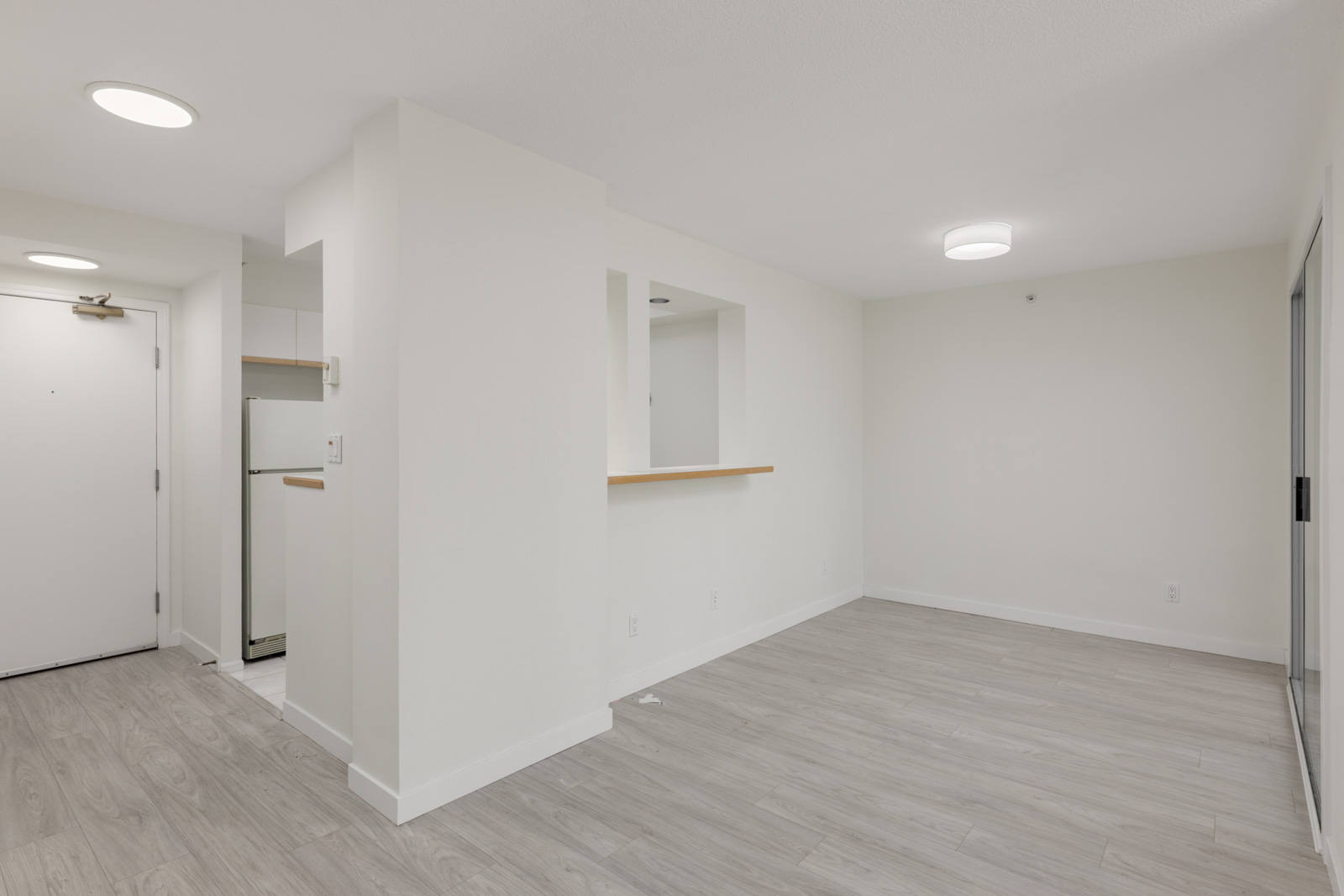 Unfurnished apartment at 950 Cambie St, Vancouver with light wood floors, white walls, open kitchen, door and fridge on the left.
