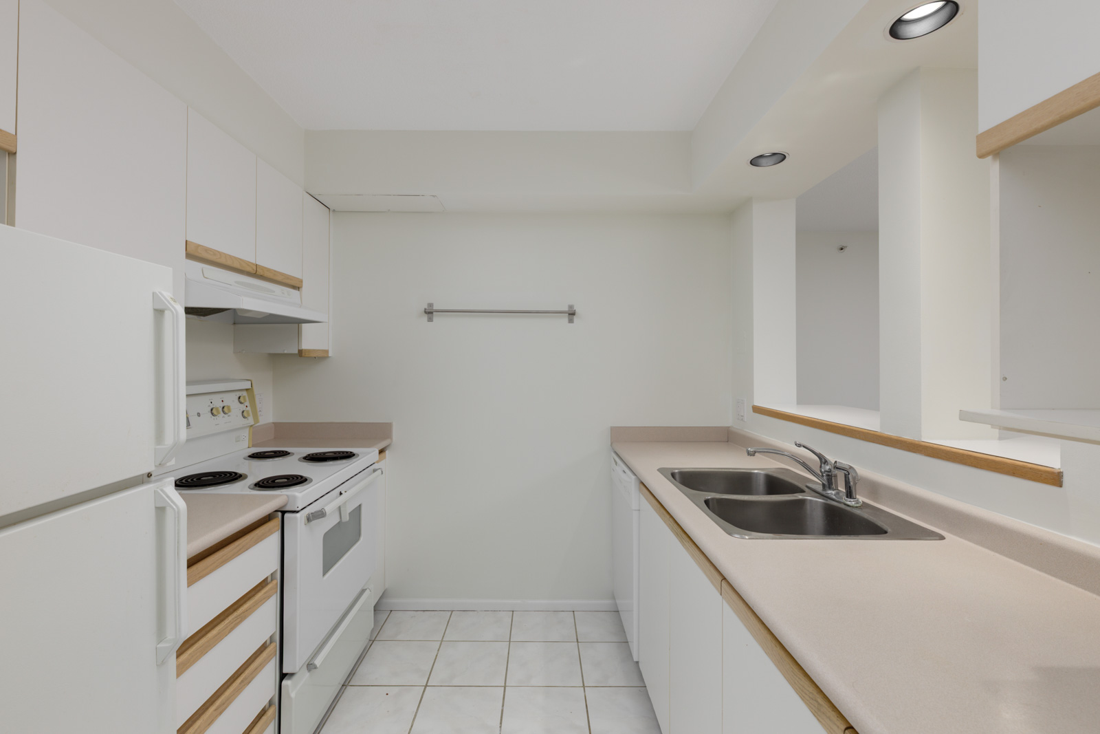 Compact kitchen at 950 Cambie St, Vancouver, with white cabinets, electric stove, double sink, beige counters, tile floor.