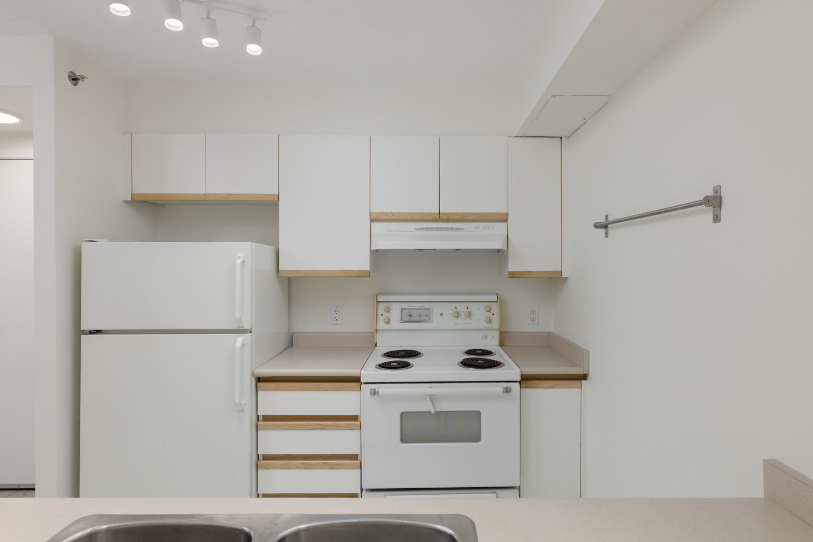 Compact kitchen at 950 Cambie St, Vancouver, with white cabinets, electric stove, fridge, beige counters, and an empty towel rack.