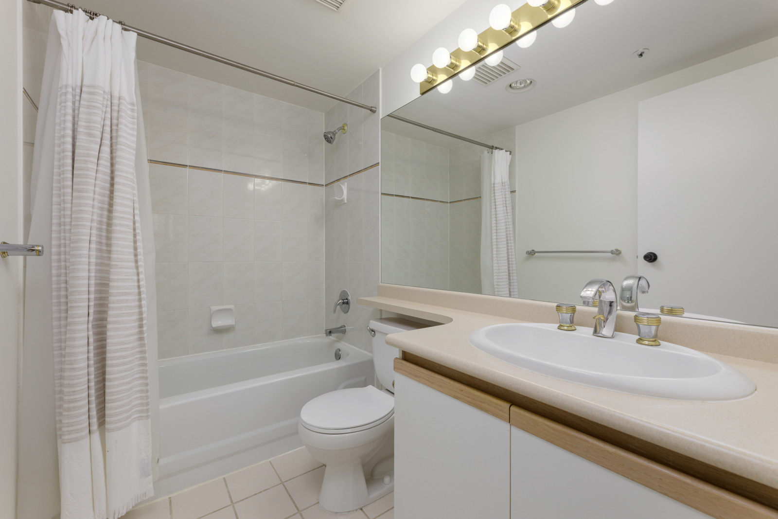 Modern Vancouver bathroom with bathtub-shower combo, white tiles, toilet, large mirror, and countertop sink at 950 Cambie St.