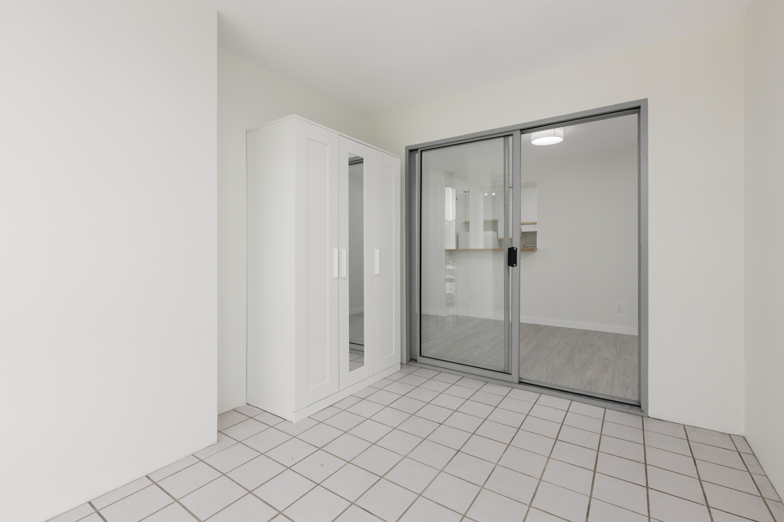 Empty room with white tile floor, mirrored white wardrobe, and glass sliding door to a light wood floor room at 950 Cambie St, Vancouver.