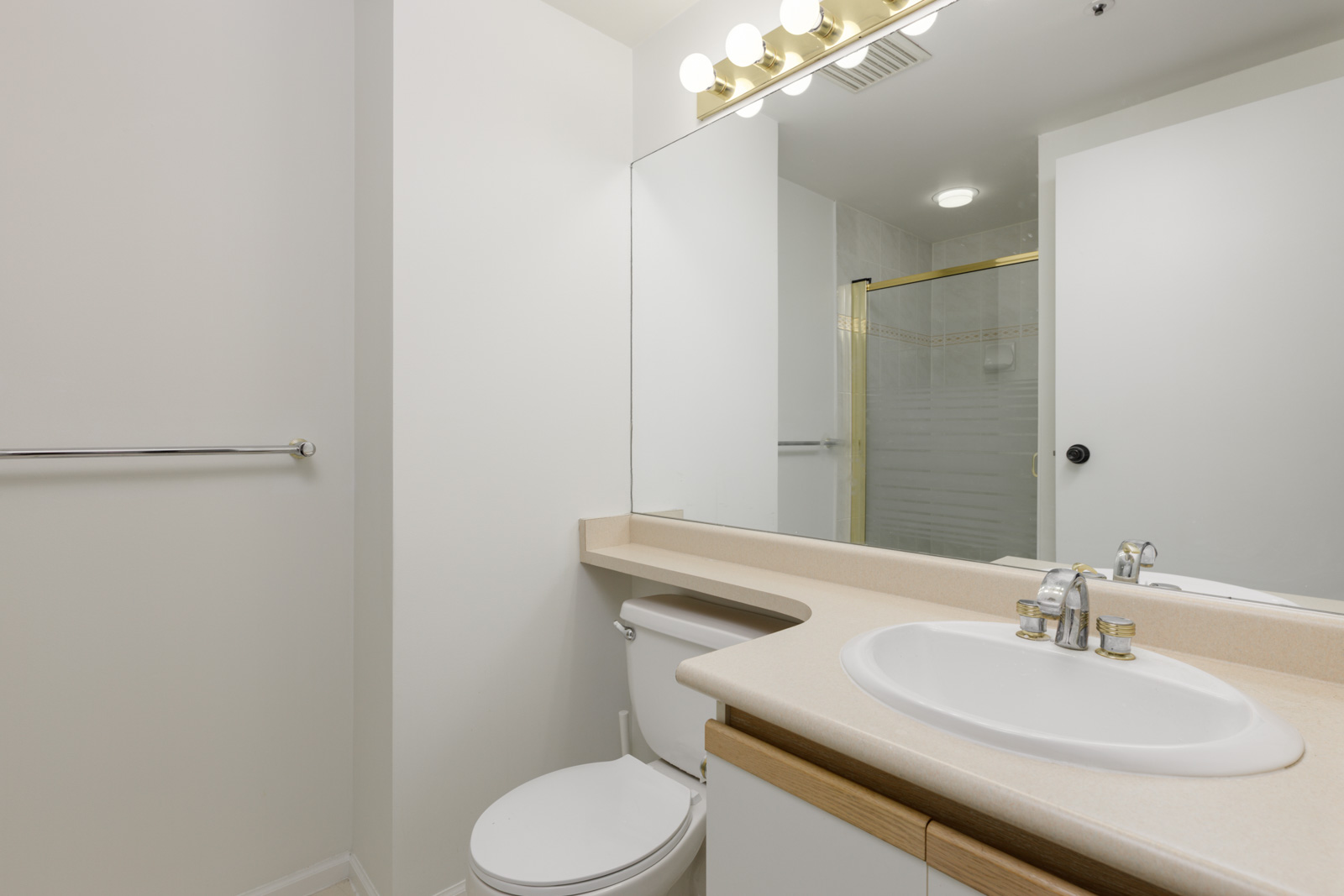 Bathroom at 950 Cambie St. with large mirror, white sink, faucet, toilet, countertop, towel bar, and glass shower enclosure.