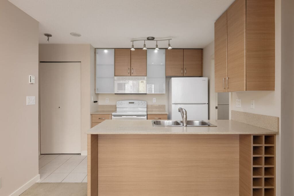 Modern kitchen on 10th floor, light wood cabinets, white appliances, island sink, wine rack; neutral walls, tile floors. Vancouver.