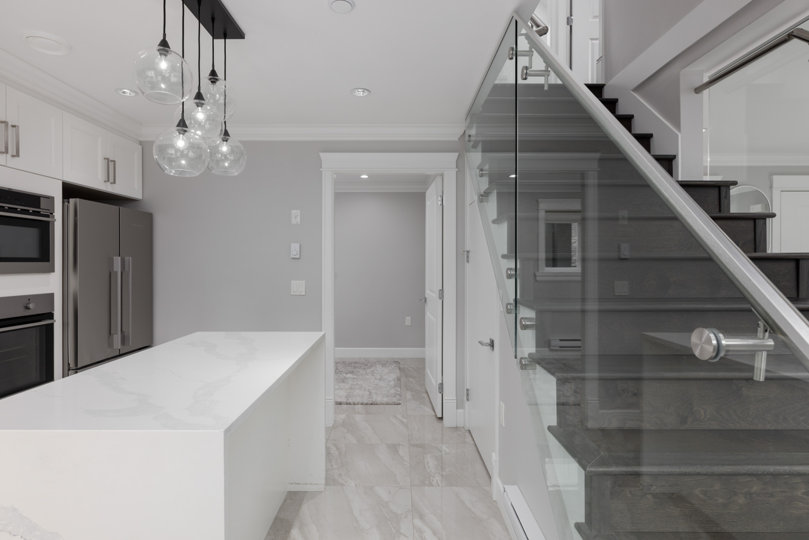 Modern kitchen with white cabinets, stainless appliances, marble island, glass railing, tiled floor in Vancouver’s Falaise Ave.