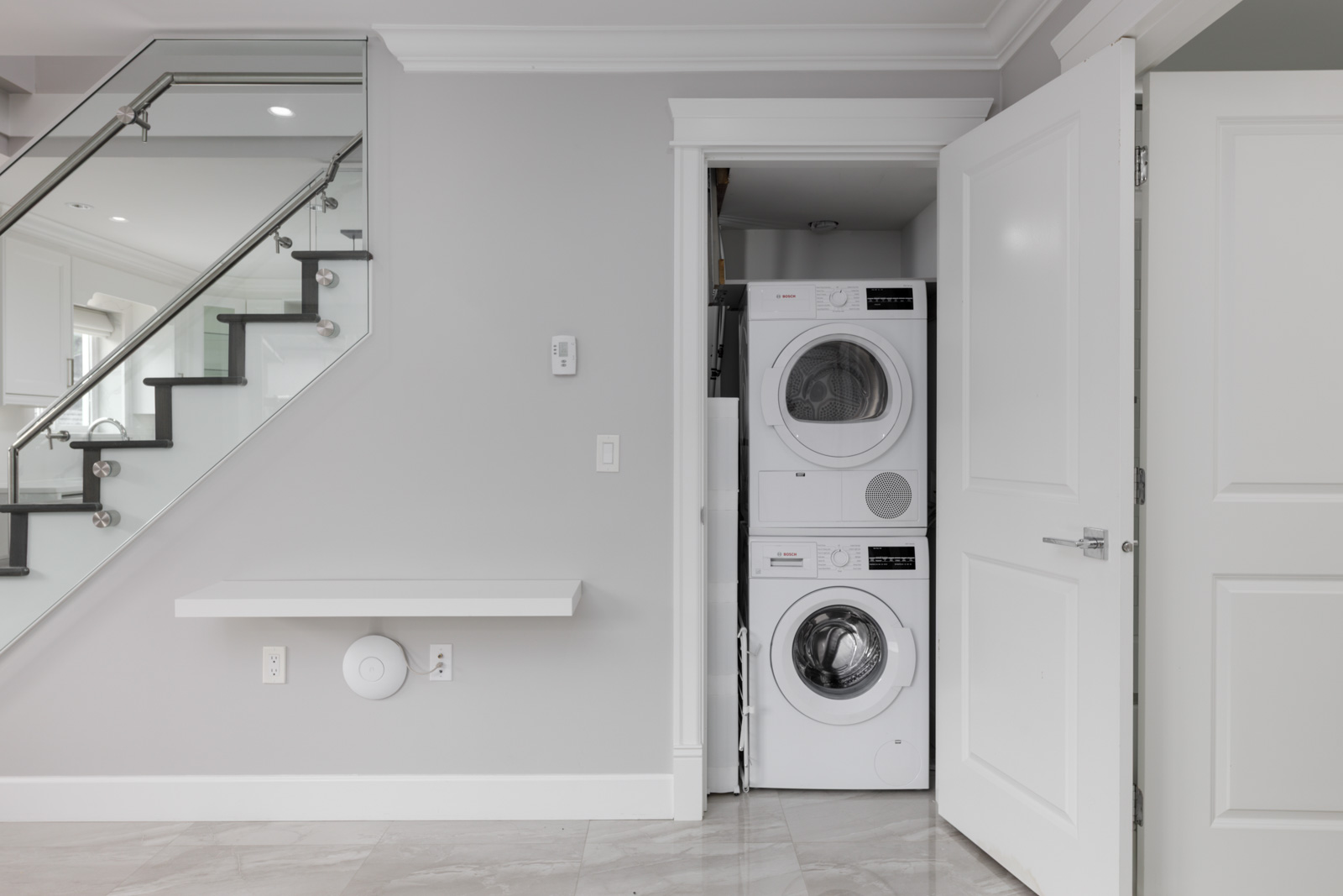 A stacked washer and dryer sit in an open closet by a staircase in a gray-walled room at Vancouver’s Falaise Place.