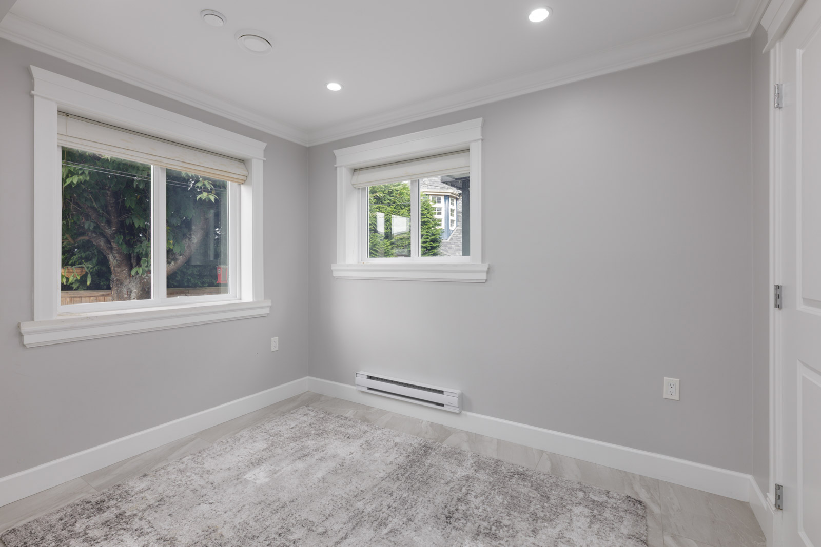 Empty room with light gray walls, two windows with blinds, white baseboard heater, and gray rug on tiled floor in Vancouver.